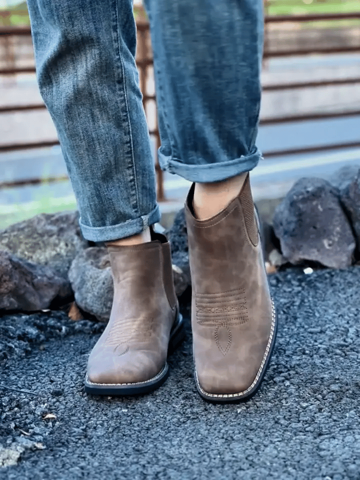 Brown ankle boots worn with rolled-up jeans on a stone surface.